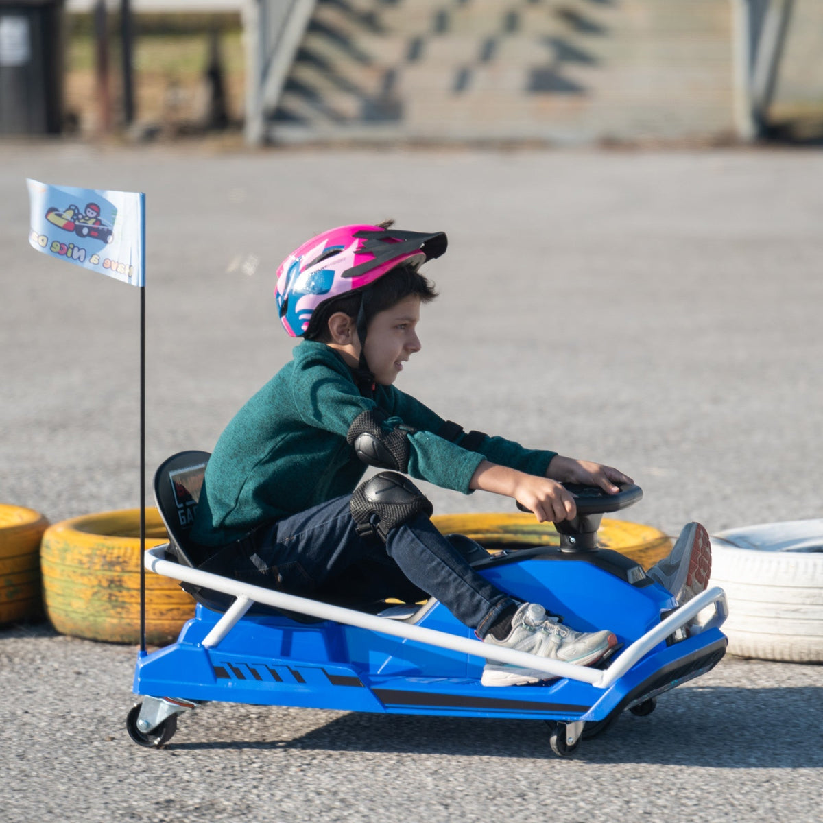 A young boy in a helmet and knee pads driving a blue KerryYoo electric drift kart on a paved go-kart track